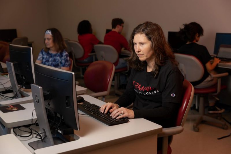Students typing at computers with student in foreground wearing Germanna Community College sweatshirt