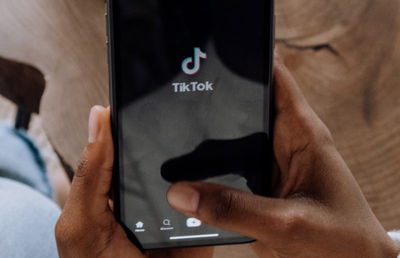 Hands holding a cellphone opening the TikTok app. Photo courtesy Pexels.