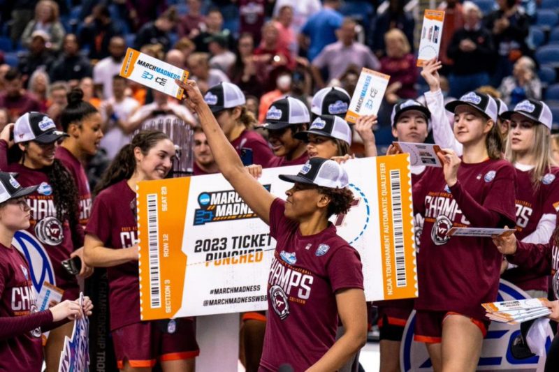 A basketball player holds up a ticket that shows the women's team will advance to plan in the NCAA tournament