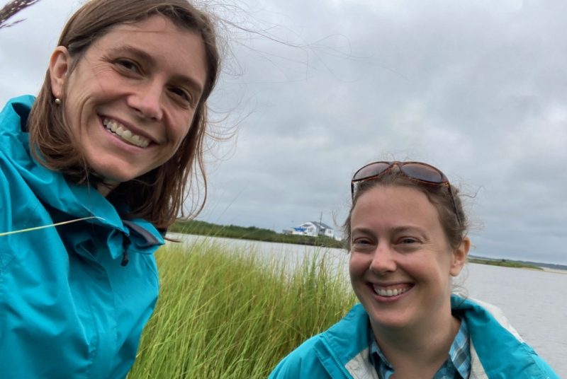 Two people stand in front of a coastal marsh on a cloudy day. 