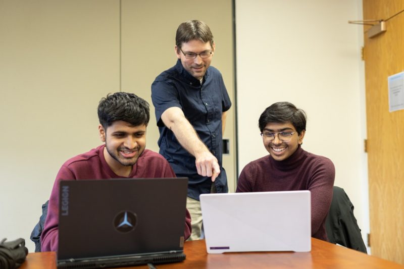 Chreston Miller, Deep Datta, and Ishana Garuda gather around a two laptop computers.