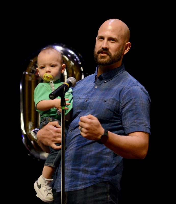A VTCSOM student stands at the microphone holding his infant son to announce his match.