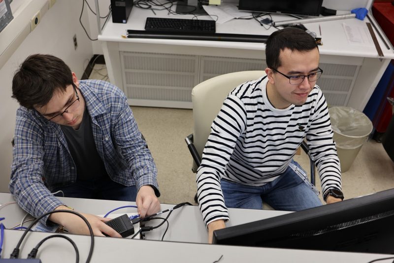 Undergraduate Thomas Wheeler (at left) and Ph.D. candidate Bruce Barbour (at right) work on the hardware-in-the-loop testbed that emulates the changing connectivity of a mega-constellation at scale. 