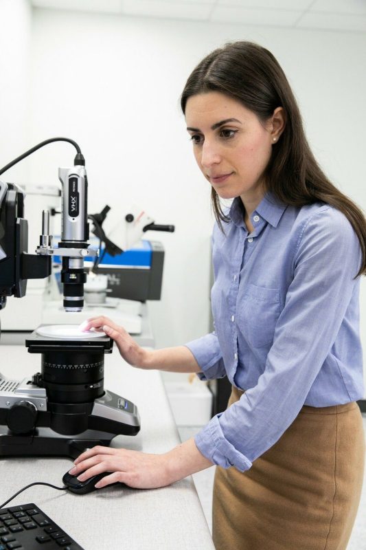 Christina DiMarino stands in front of a microscope.