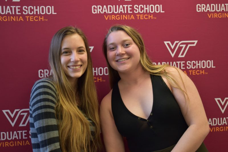 Rose Campbell and Emily Tirrell in front of a Graduate School banner