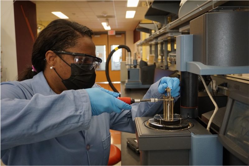 Tiffany Thompson uses a handheld tool to adjust a small, metallic laboratory instrument.