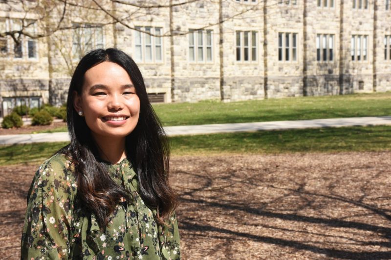 A woman with long black hair and a flower print blouse poses near a Hokie Stone building.