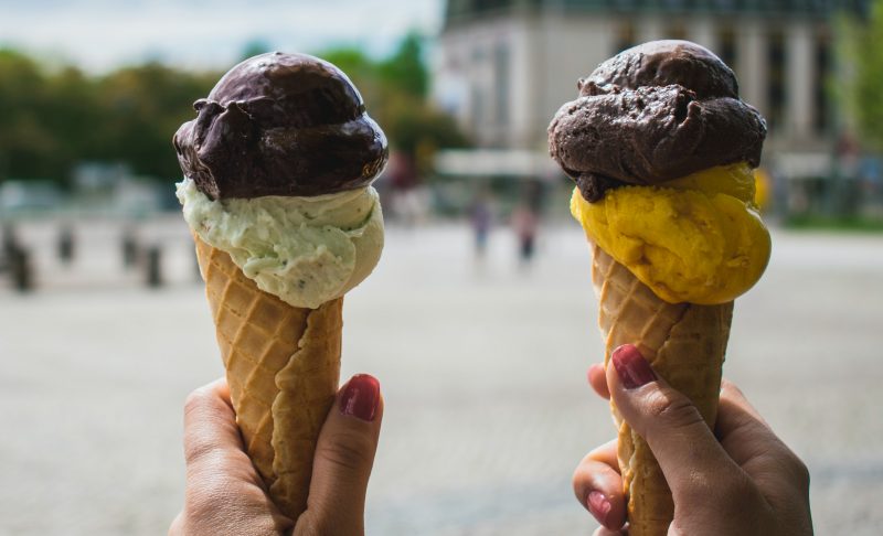Outdoors scene with hands holding two ice cream cones. Photo courtesy Pexels.