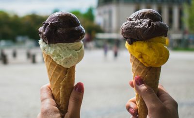 Outdoors scene with hands holding two ice cream cones. Photo courtesy Pexels.