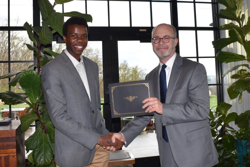 Victor Mukora shakes hands with, and receives a certificate from, Mark Embree.