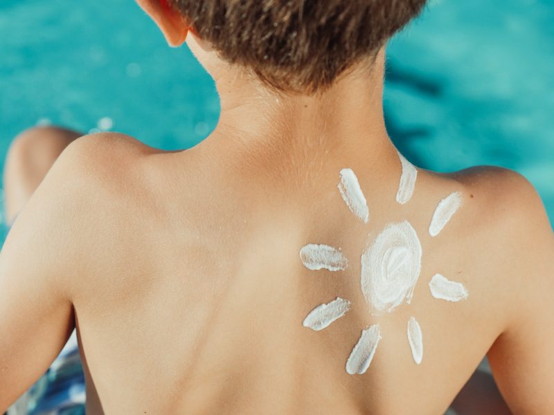 A boy with a sun drawn with sunscreen on his back. Image courtesy Pexels.