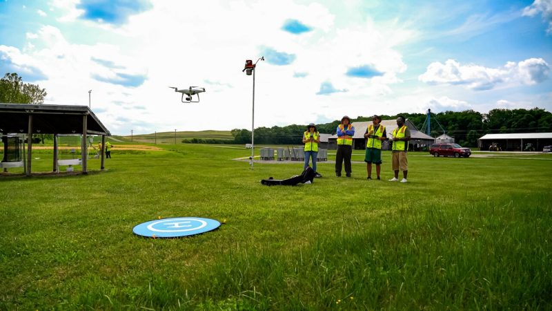 A teacher kneels down in front of a drone on a launchpad.