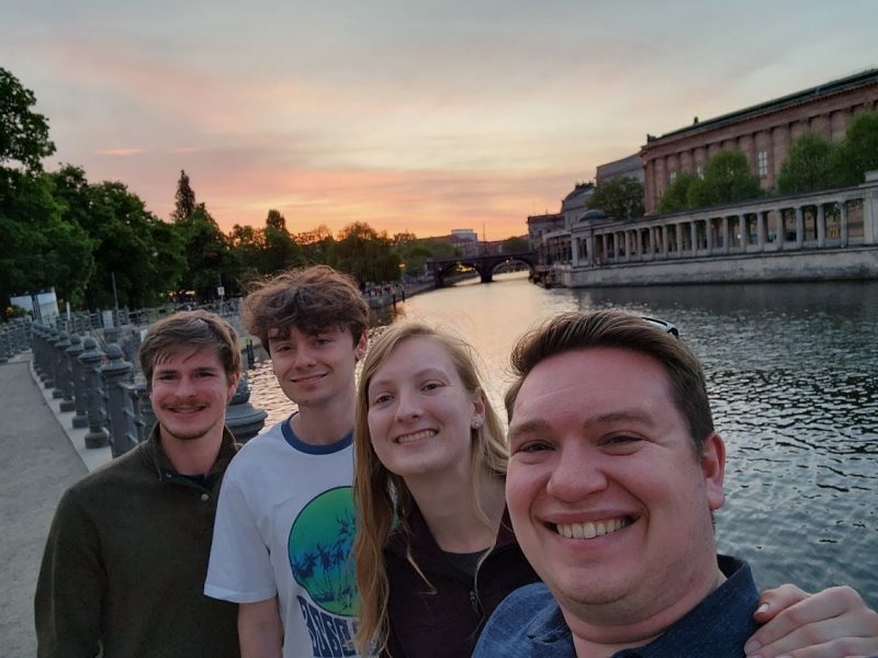 students stand in front of river with sunsetting in the background