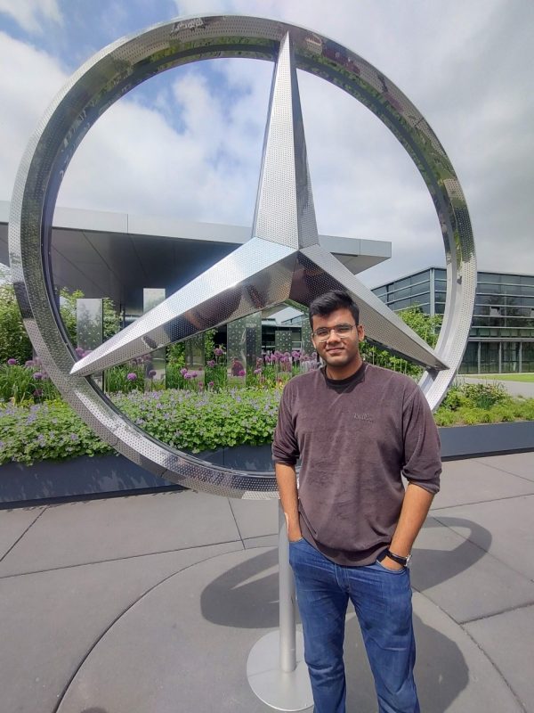 student poses in front of mercedes benz logo.