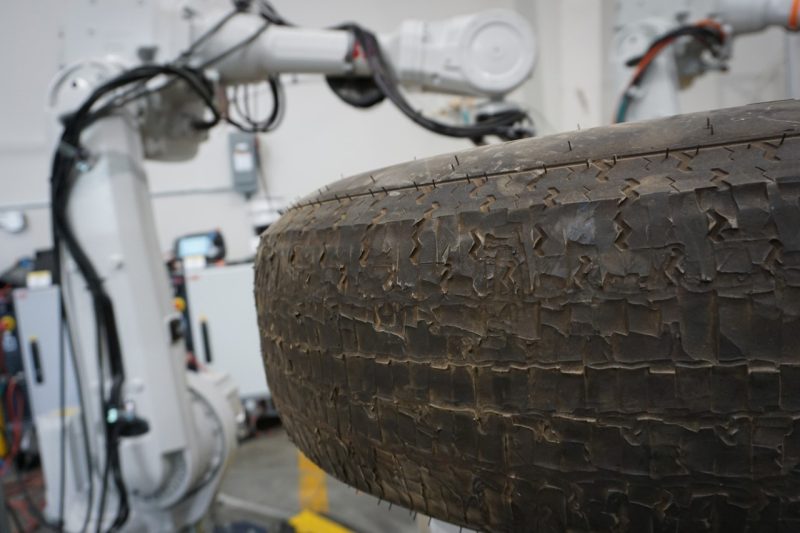 The tread of a large vehicle tire can be seen close up, with imperfections in the pattern that indicate the tire has been worn down. 