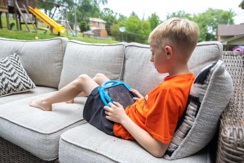 Child sitting on an outside couch playing on his IPad.