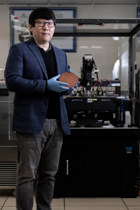 faculty member holds a semiconductor wafer in a lab while looking at the camera