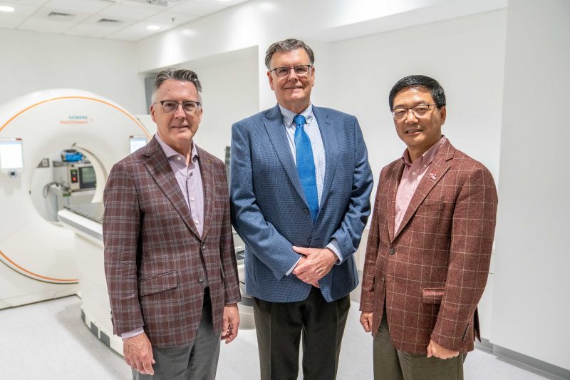 Virginia Tech President Tim Sands, Vice President for Health Sciences and Technology Michael Friedlander and Senior Vice President for Research and Innovation Dan Sui pose in front of a CT scanner used for diagnostic and radiation treatment planning. Virginia Tech photo by Clayton Metz.