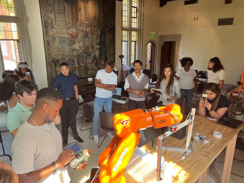 Students gather around robotic arm.