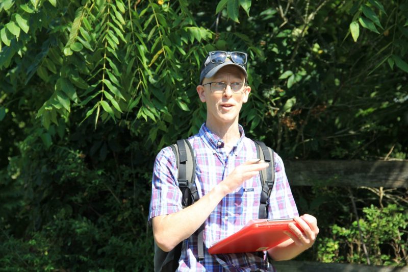 Leighton Reid in a checkered patterned button up shirt outside in the sun.