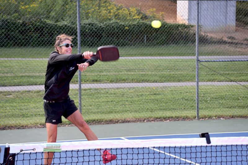 A woman in a black sports outfit hits a pickleball on a court at a city park.