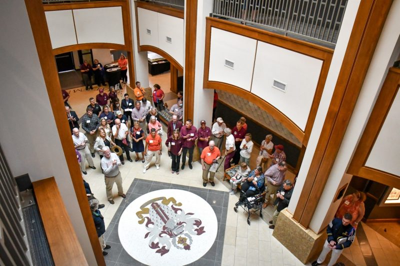 A view from the second floor of a large group of people gathering near the corps crest mosaic on the floor of the main atrium on the first floor. 