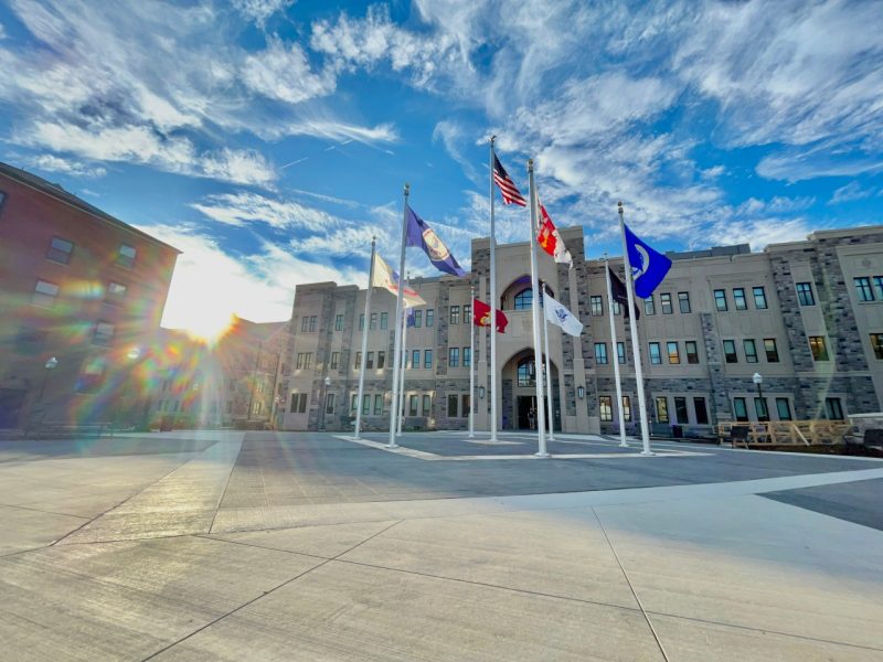 Low-angle image of the front of the building against a blue sky and wispy clouds. The flags are illuminated by the setting sun and blowing in the breeze.
