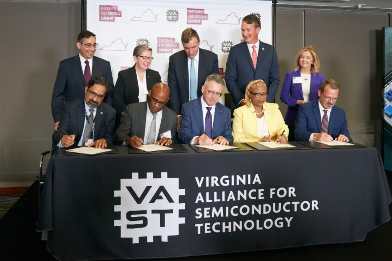Ten people pose for a photo during the signing of a memorandum of understanding for the Virginia Alliance for Semiconductor Technology during the CHIPS for Virginia Summit.