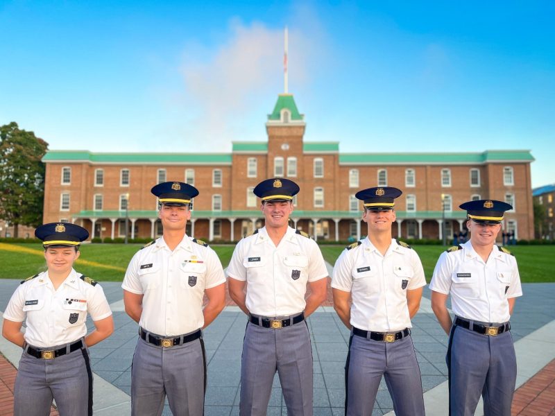 The five cadets are in their white shirt uniforms on Upper Quad. They are smiling and Lane Hall is behind them.