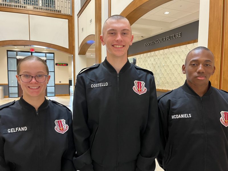 Cadets in black uniform jackets stand smiling inside the atrium of the Corps Leadership and Military Science Building.