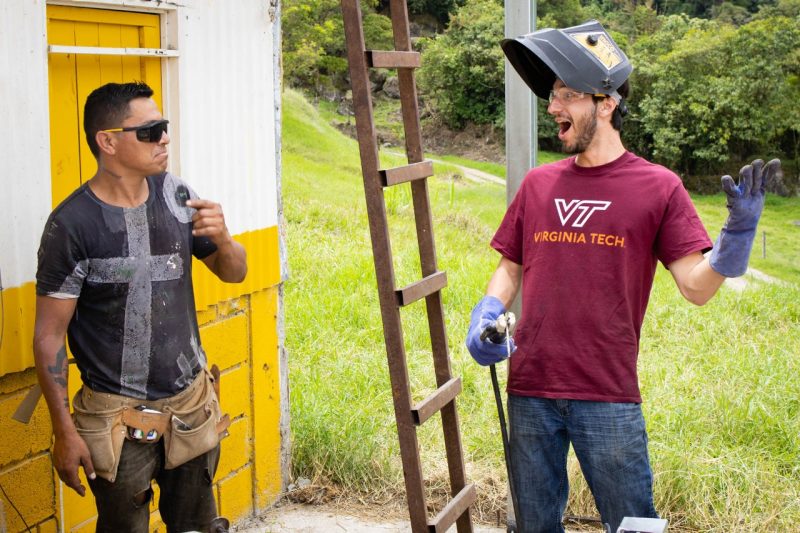 A contractor stands to the left with a Virginia Tech student to the right smiling after completing a successful weld.