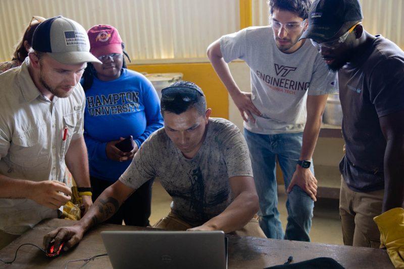Four students stand around Dario Bravo looking at a laptop screen.