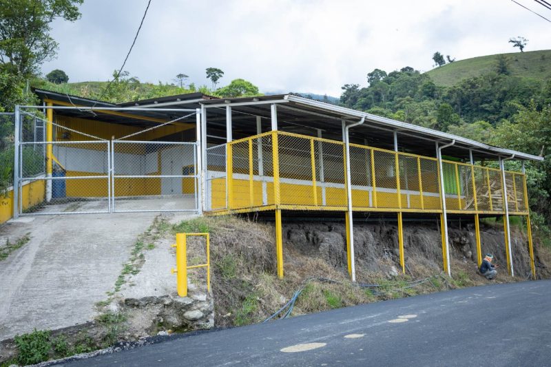 A yellow and white community center sits on a hill with a large, new gate creating added security.