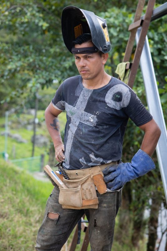 Dario Bravo, a Costa Rican contractor, stands with his hands on his hips looking off to the distance with a ladder behind him.