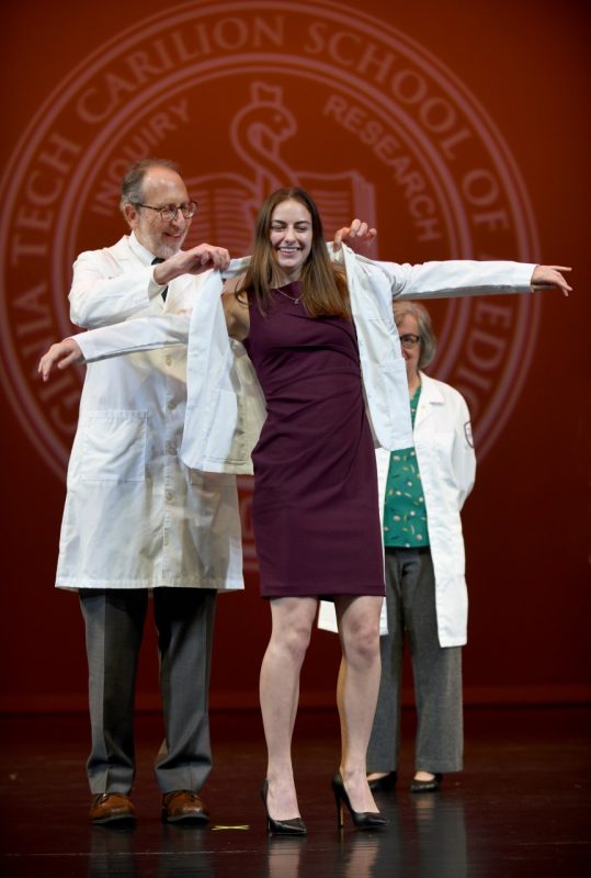 Dean Lee Learman helps first-year student Audrey Korte put on her white coat. 