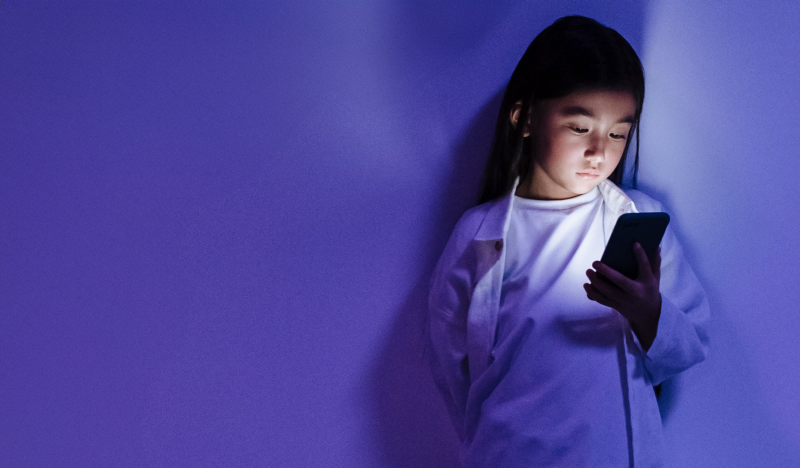 A young girl looking at the screen of a smartphone.