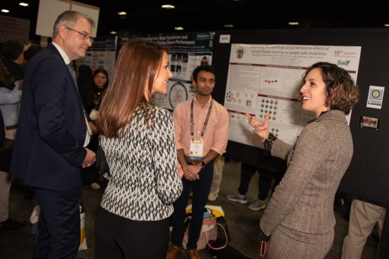 A group of people engage in discussion in front of a research poster at a conference.