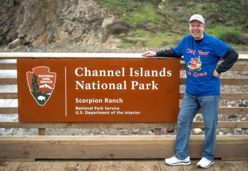 man standing beside national parks sign