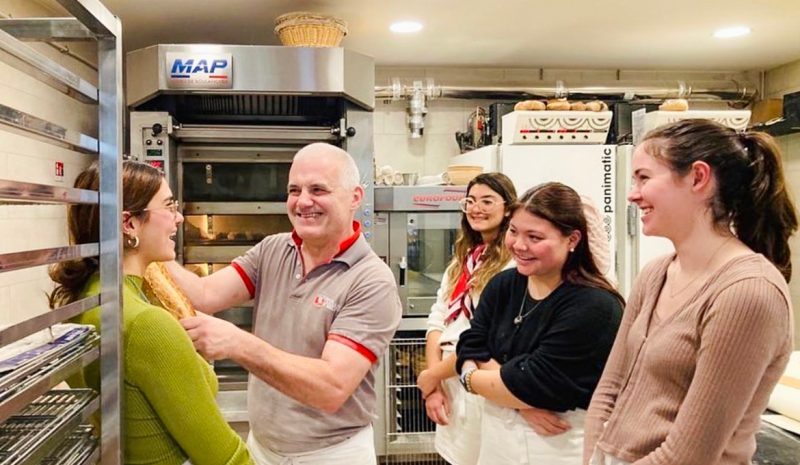 A baker showing a baguette to a group of students in his bakery