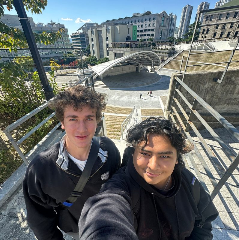 Two students posing for a selfie in front of an amphitheater