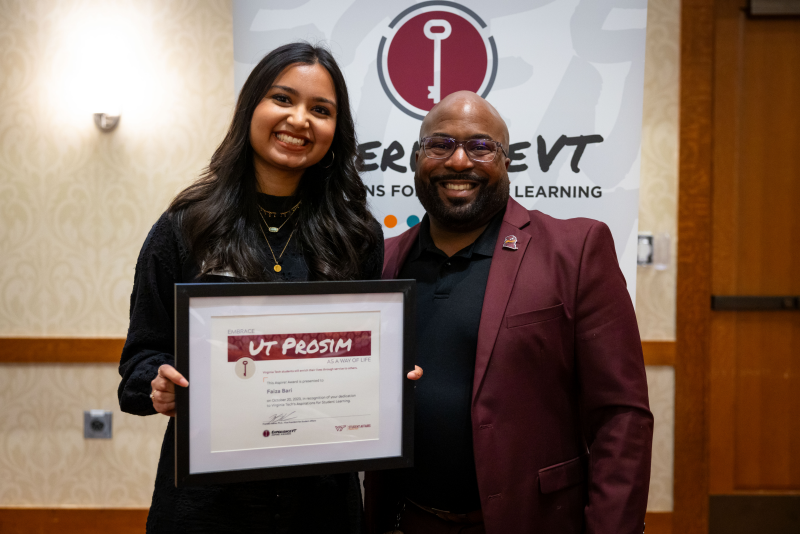 Faiza stands to the left of Assistant Vice President of ExperienceVT, James Bridgeforth, holding her award.