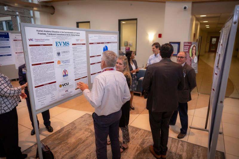 Faculty from the Virginia Tech Carilion School of Medicine discuss research posters standing in the school's lobby.