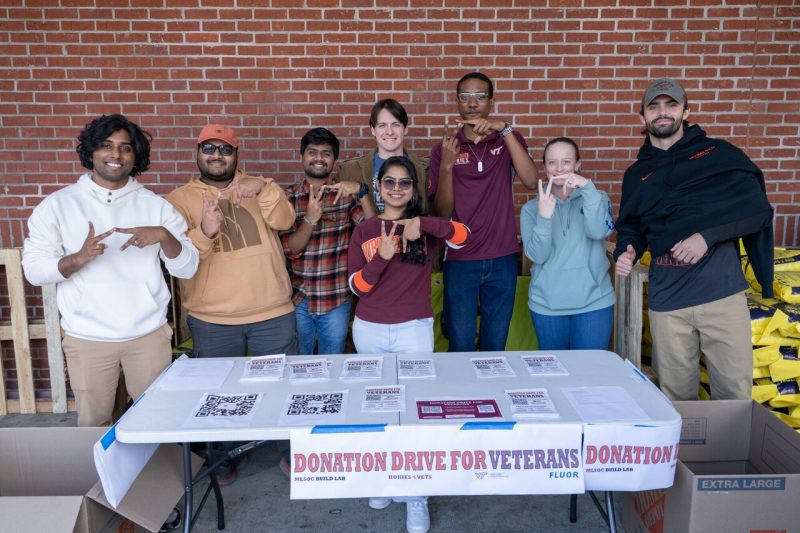 Virginia Tech graduate students stand in front of Virginia Tech for Veterans table while making the VT sign.