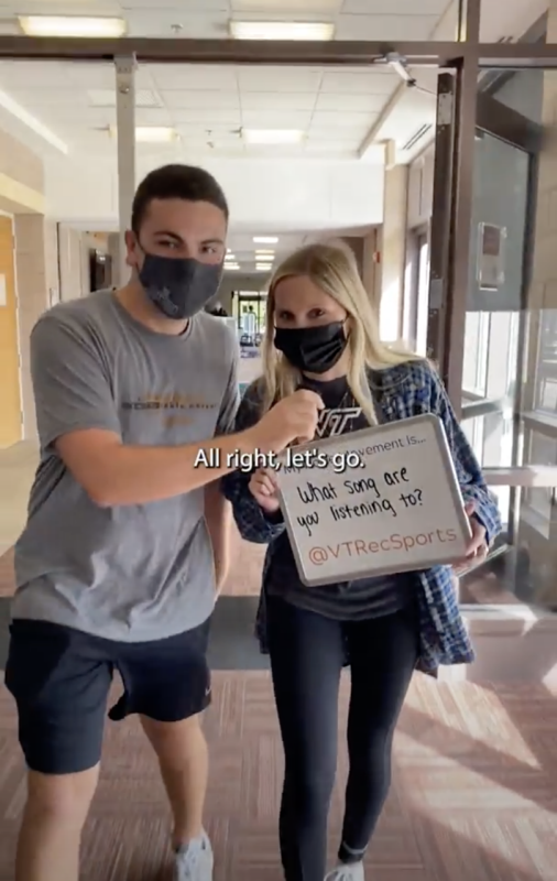 Jackson and Caroline walk through a door while holding a white board sign that says what song are you listening to?