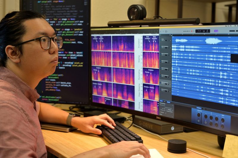James Chen sits in front of three large computer screens showing sound wave data.