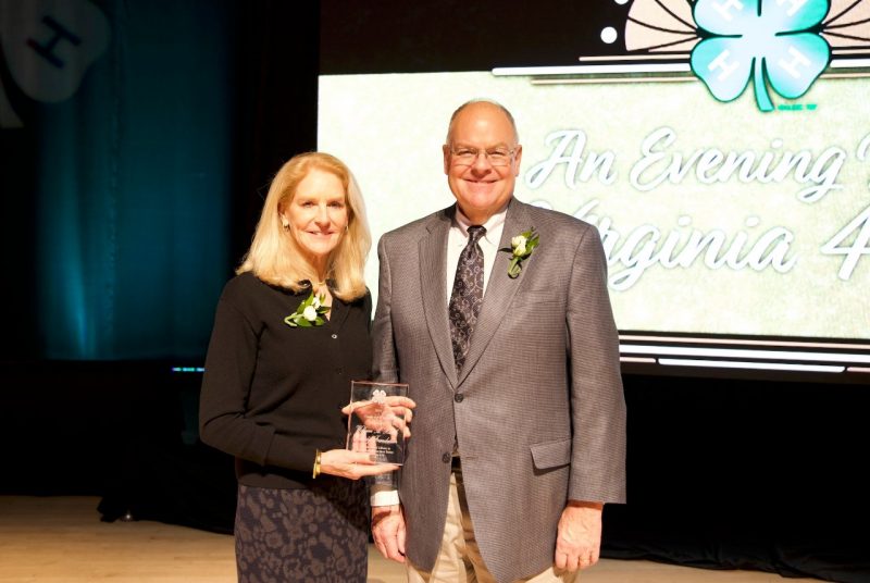 A woman holding a glass award stands next to a man in front of a sign that reads, "An Evening with Virginia 4-H."
