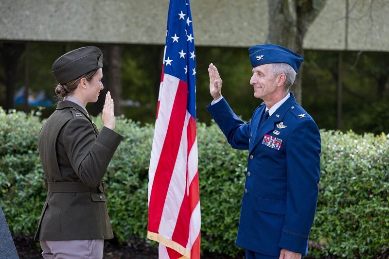 Maddie Nardi, in full military dress, takes an oath with a senior officer in front of an American flag