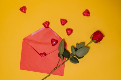 Red rose sitting next to envelope and hearts 