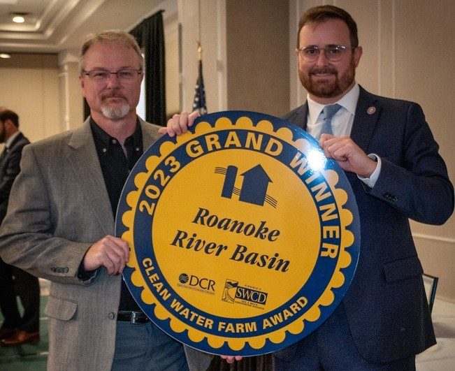 Two men hold a large circular award that says "2023 Grand Basin Winner," posing for the camera.