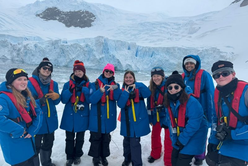  A group of people stands in front of a large glacier of ice.